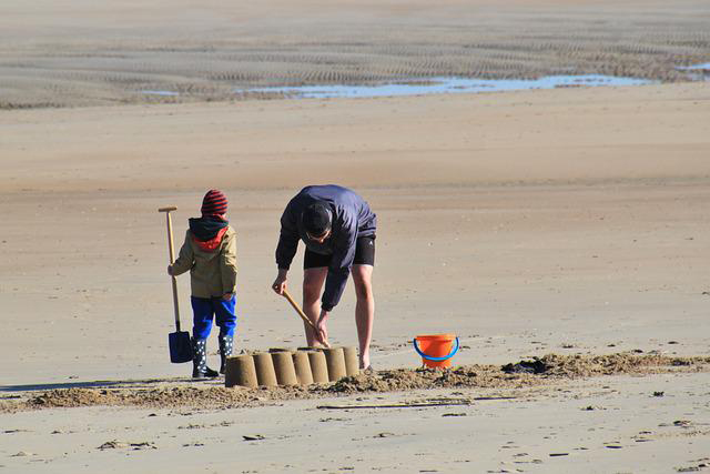 Two people on beach with sand bucket piles